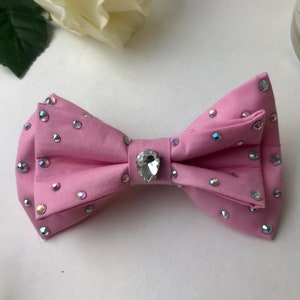 May include: A pink bow tie with a large clear rhinestone in the center and smaller rhinestones scattered across the fabric.