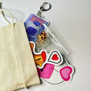 May include: A white canvas bag with a keychain attached. The keychain features a blue and white cartoon character, a yellow and orange cartoon character, and a pink heart. The blue and white character has the Japanese text "スイッチ" on it.