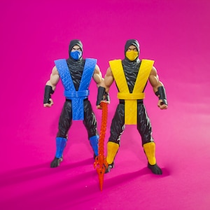 Peut inclure: Deux figurines d'action de ninjas, l'une en bleu et l'autre en jaune, tenant une arme rouge et orange. Les figurines sont en position de combat.
