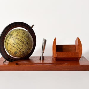 May include: A vintage wooden desk organizer featuring a globe, pen, and pen holder. The globe is mounted in a dark brown ring with degree markings. The pen is silver, and the pen holder and organizer are made of reddish-brown wood.