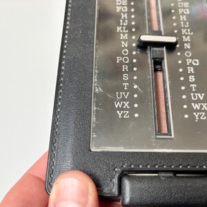 Puede incluir: Un directorio telef&oacute;nico negro con un &iacute;ndice deslizante de pl&aacute;stico transparente. El &iacute;ndice est&aacute; etiquetado con letras de DE a YZ. El libro est&aacute; sostenido por una mano.