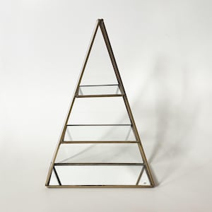 May include: A pyramid-shaped display shelf with a bronze-colored metal frame and clear glass shelves. The geometric design features four horizontal shelves within the triangular structure. The shelves are ideal for displaying small items.