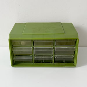 May include: A rectangular olive green plastic storage organiser featuring nine individual clear pull-out drawers arranged in a three-by-three grid. The unit has a solid top surface and a sturdy frame, designed for sorting small items and components.