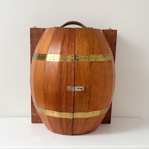 Peut inclure: Une armoire en bois en forme de tonneau avec une fente verticale au centre, dotée de deux bandes horizontales en laiton et d'un loquet métallique central. L'armoire est fixée sur un panneau arrière rectangulaire et possède une poignée.