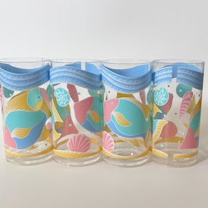 May include: Four clear drinking glasses with a sea life design. Each glass has a blue wave pattern at the top and colourful illustrations of fish, seashells, and coral in teal, pink, and yellow.