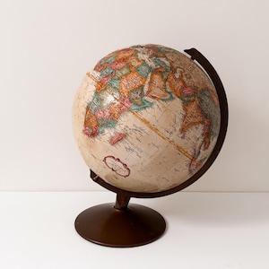 May include: A vintage globe with a cream-coloured surface, showing colourful continents and countries. It's mounted on a dark brown metal stand with a circular base and a curved support. A decorative item for the home.