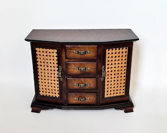 May include: A dark brown wooden jewelry box with four drawers and two side doors with woven cane inserts. The box has ornate brass hardware and a curved top and base. The jewelry box is on a white background.