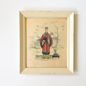Könnte beinhalten: Gerahmter Vintage-Druck mit einer Figur in traditioneller asiatischer Kleidung. Das Kunstwerk zeigt eine Person in einem roten Gewand mit schwarzen und grünen Akzenten, vor dem Hintergrund einer Landschaft mit Bäumen und Bergen. Der Rahmen ist cremefarben.