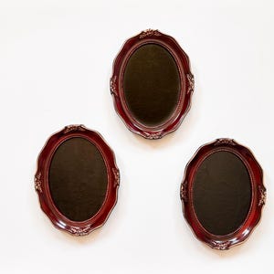 Peut inclure: Trois cadres photo ovales, de couleur rouge foncé, avec des détails dorés ornés. Les cadres ont un bord festonné et un intérieur marron foncé. Ils sont présentés sur un fond blanc. Parfaits pour afficher des photos ou des œuvres d'art.