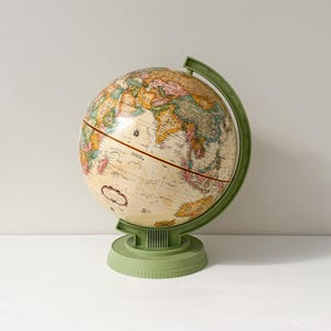 May include: A world globe featuring a cream-coloured map with multicoloured continents and oceans. The globe is mounted on a sage green plastic stand with a curved meridian arm and a circular base. A horizontal line divides the sphere in half.