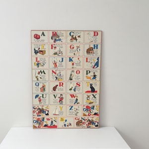 May include: A rectangular wall poster featuring a vintage alphabet grid with letters A through Z. Each letter is accompanied by a colourful illustration and a short descriptive sentence. The design includes various characters, animals, and objects.
