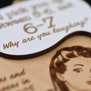 May include: A wooden plaque with engraved text and a vintage-style illustration. The plaque features a speech bubble with the words "Why are you laughing?" and other text. The illustration is of a woman's face.