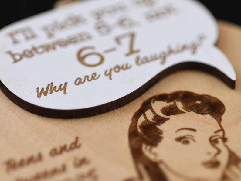 May include: A wooden plaque with engraved text and a vintage-style illustration. The plaque features a speech bubble with the words "Why are you laughing?" and other text. The illustration is of a woman's face.