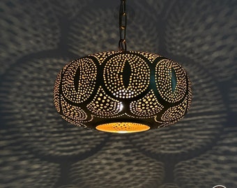 May include: A black metal pendant light with a round, ornate design. The light has a geometric pattern of circles and ovals, and it is illuminated from within.