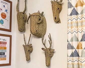 May include: A white wall with four woven animal head wall decor pieces. The decor is made of natural materials and has a rustic look. The wall decor is hung above a white couch with green and blue pillows. The wall also has a framed print with the text "Today I Will: Stay Positive, Learn & Grow, Worry Less, Say Kind Words, Laugh More, Choose Love, Believe in Myself".