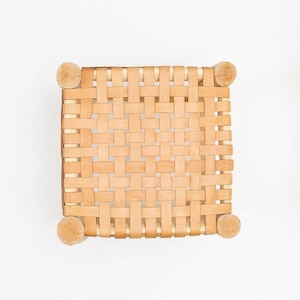 May include: A square woven leather stool with a natural tan colour. The stool has four wooden legs.