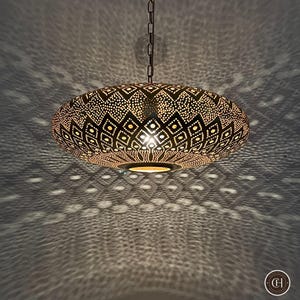 Peut inclure: Un grand luminaire suspendu rond en laiton avec des motifs géométriques complexes et une chaîne suspendue au plafond. Le luminaire projette une ombre sur le plafond en dessous.