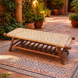 Könnte beinhalten: Gewebte Bank mit Sitzfläche aus Naturfaser und Holzrahmen. Die Bank ist rechteckig und hat ein Lattenregal darunter. Die Bank ist ca. 122 cm lang und 46 cm breit. Die Bank befindet sich im Freien auf einer gemusterten Fliesenoberfläche.