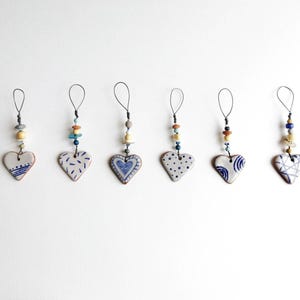 May include: Seven handmade ceramic heart ornaments with blue and white patterns and colourful beads hanging from a wire loop.