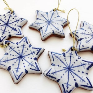 May include: Five white ceramic star ornaments with blue snowflake designs and gold string hangers.