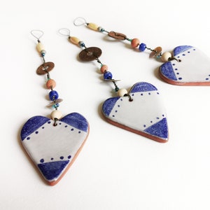 May include: Three ceramic heart ornaments with blue and white geometric designs, each hanging from a string of beads and charms.