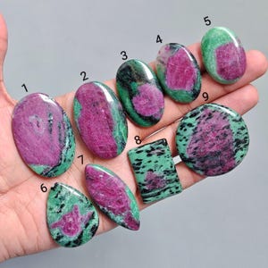 May include: A selection of polished ruby zoisite gemstones in diverse forms, such as oval, teardrop, and rectangular. The stones showcase a blend of vivid pink and green hues, with the pink ruby set against the green zoisite.