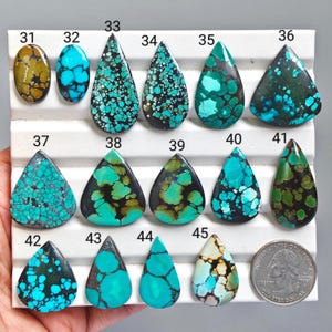 Può includere: Una collezione di quindici cabochon di turchese lucidati di varie forme e motivi, numerati da 31 a 45, esposti su un vassoio bianco scanalato accanto a una moneta da un quarter statunitense per la scala, con matrice blu, verde e marrone.