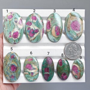 May include: Nine oval-shaped ruby in fuchsite cabochons arranged on a white display tray, numbered one through nine. Each stone features a mix of vibrant magenta-pink ruby inclusions set within a green and white mineral matrix, alongside a US quarter.