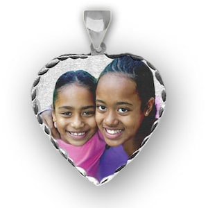 Op de afbeelding: Zilveren hartvormige hanger met een foto van twee jonge meisjes die lachen. De hanger heeft een gegolfde rand.