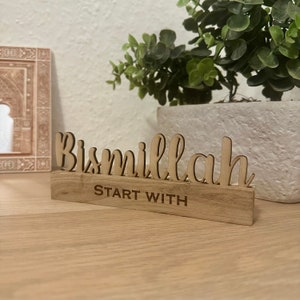 Op de afbeelding: Een houten bord met de Arabische zin "Bismillah" in cursief schrift, en de woorden "Start With" eronder.