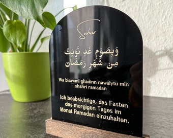 May include: A black acrylic sign with a gold inscription in Arabic and English. The sign reads "Wa bisawmi ghadinn nawaiytu min shahri ramadan" and "Ich beabsichtige, das Fasten des morgigen Tages im Monat Ramadan einzuhalten."