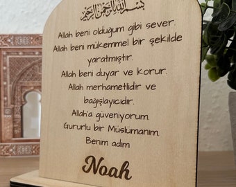 May include: A wooden plaque with an arched top and a stand. The plaque has an inscription in Arabic script and text in Turkish. The text reads "Allah beni olduğum gibi sever. Allah beni mükemmel bir şekilde yaratmıştır. Allah beni duyar ve korur. Allah merhametlidir ve bağışlayıcıdır. Allah'a güveniyorum. Gururlu bir Müslümanım. Benim adım Noah".