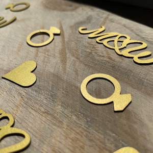 May include: Gold glitter paper cutouts of a heart, rings, and the word "Mr & Mrs" on a wooden surface.