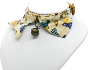 May include: A white and beige cat collar with a bell and a yellow button. The collar has a pattern of small birds and chicks.