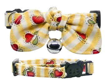 May include: Yellow and white striped cat collar with a red heart pattern and a bow tie. The collar has a bell and a safety buckle.