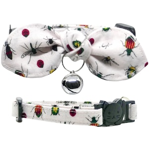 May include: White cat collar with a bow tie and a bell. The bow tie has a bug print with red, green, and yellow bugs. The collar has a black cat head buckle.