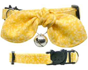 May include: Yellow cat collar with a floral pattern and a bow. The collar has a bell and a safety buckle with a cat face.