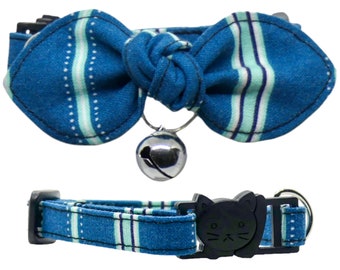 May include: A blue and white striped cat collar with a bow tie and a bell. The collar has a black plastic buckle with a cat face design.