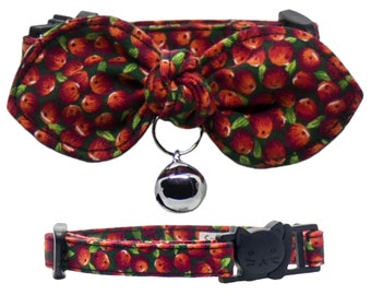 May include: A red and green cat collar with a bow and a bell. The collar has a small cat face buckle.