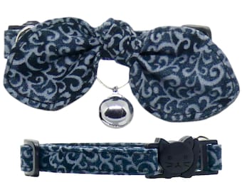 May include: A blue and silver cat collar with a bow tie and a bell. The bow tie has a paisley pattern. The collar has a safety buckle.