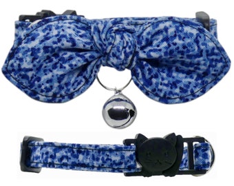 May include: Blue and white patterned cat collar with a bow and a silver bell. The collar has a black buckle with a cat face design.
