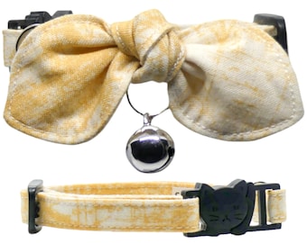 May include: A yellow and white patterned cat collar with a bow and a silver bell. The collar has a black plastic buckle with a cat face design.