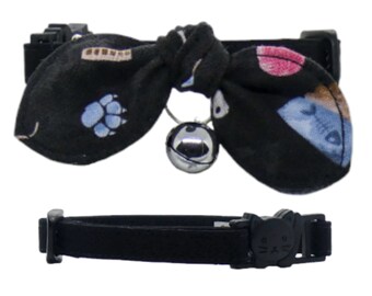 May include: Black cat collar with a black bow tie featuring a paw print, fish, and other cat-themed designs. The bow tie has a silver bell attached.