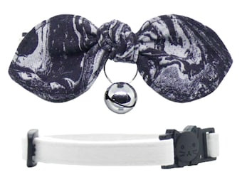 May include: A white cat collar with a black cat face buckle and a black and white marble patterned bow tie with a silver bell.
