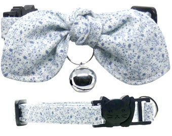 May include: A blue and white floral patterned cat collar with a bow and a silver bell. The collar has a black plastic buckle with a cat face design.