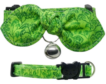 Op de afbeelding: Groene kattenhalsband met een strik en een bel. De strik is gemaakt van een groene stof met een bloemenpatroon. Het halsband is verstelbaar en heeft een veiligheidssluiting.