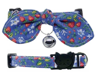 Op de afbeelding: Een blauwe kattenhalsband met een bloemenpatroon en een strik. De halsband heeft een veiligheidssluiting en een bel.