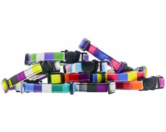 Può includere: Una collezione di collari per gatti a righe colorate con una fibbia nera a forma di testa di gatto. I collari sono in tessuto e presentano una varietà di colori, tra cui rosso, arancione, giallo, verde, blu, viola e bianco.