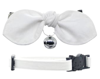 May include: White cat collar with a white bow and a silver bell. The collar has a black buckle with a cat face design.