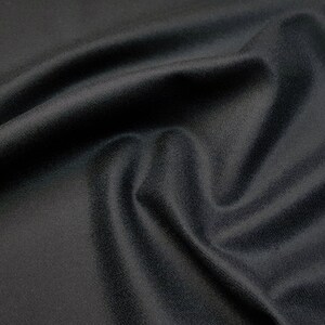 Puede incluir: Un primer plano de una tela negra con una textura suave y lisa. La tela est&aacute; drapeada y doblada, creando una sensaci&oacute;n de profundidad y dimensi&oacute;n.